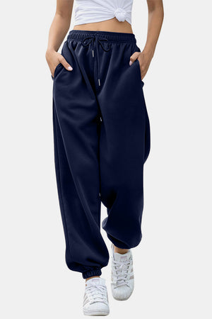 Navy sweatpants with gathered cuffs and drawstring waist, styled with white sneakers.