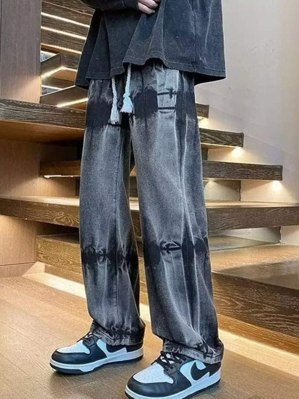 Men's black distressed vintage wash wide-leg jeans with cinched ankles and drawstring.
