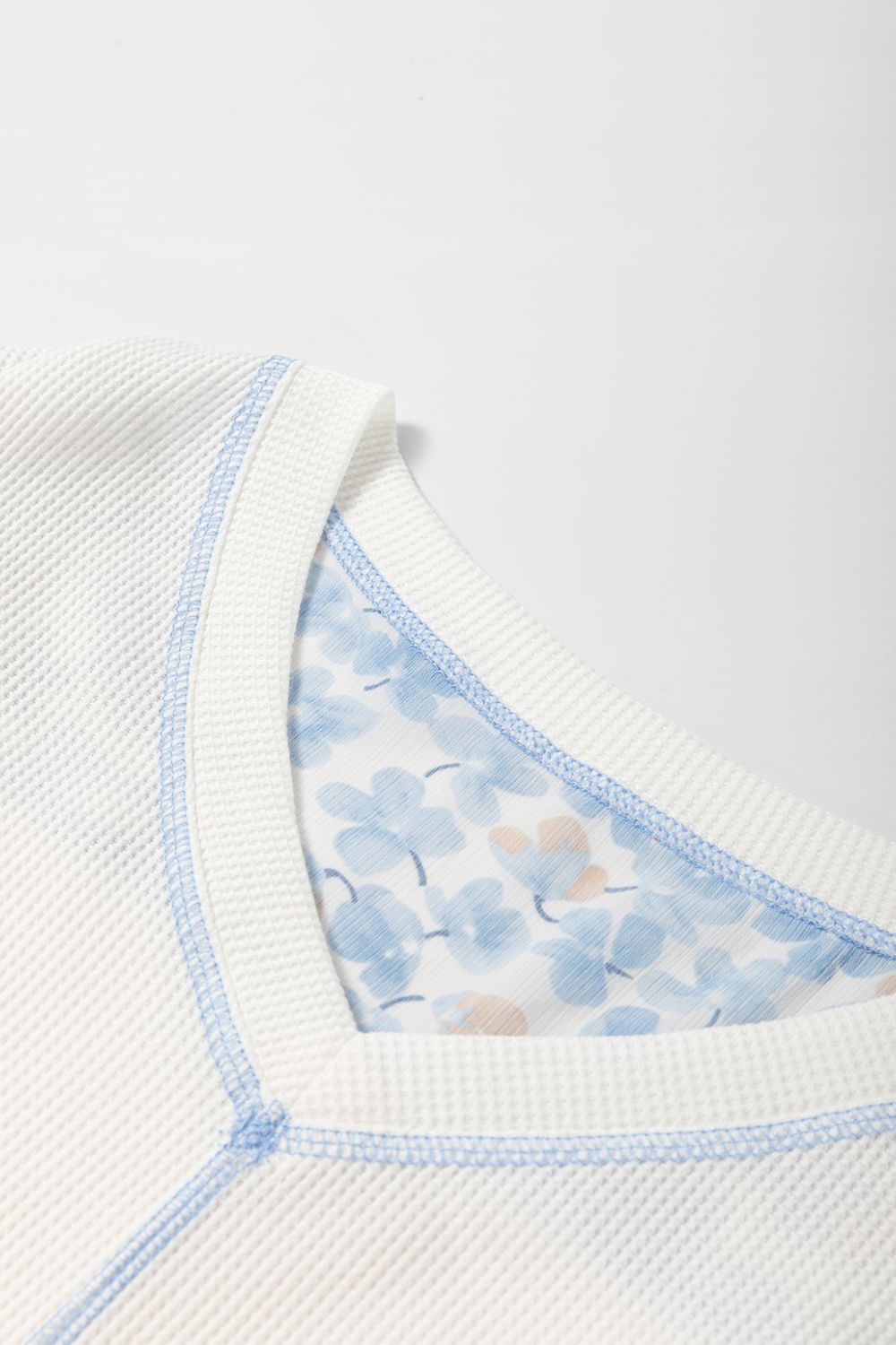 White waffle knit blouse with blue floral print lining and contrast stitching.