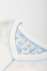 White waffle knit blouse with blue floral print lining and contrast stitching.