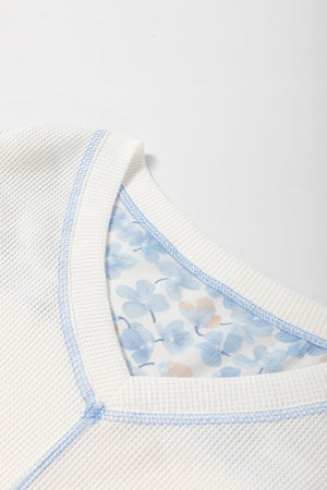 White waffle knit blouse with blue floral print lining and contrast stitching.