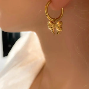 Gold hoop earrings with a dangling 18K gold-plated bow charm.