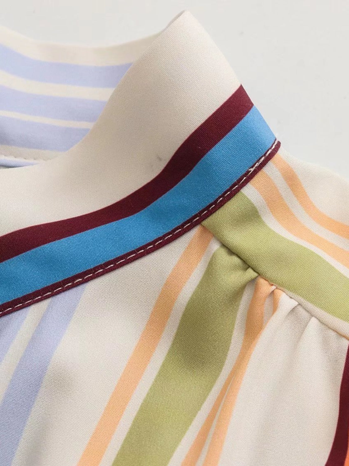 Prismatic stripe band collar blouse with multicolor stripes and blue, maroon trim detail.