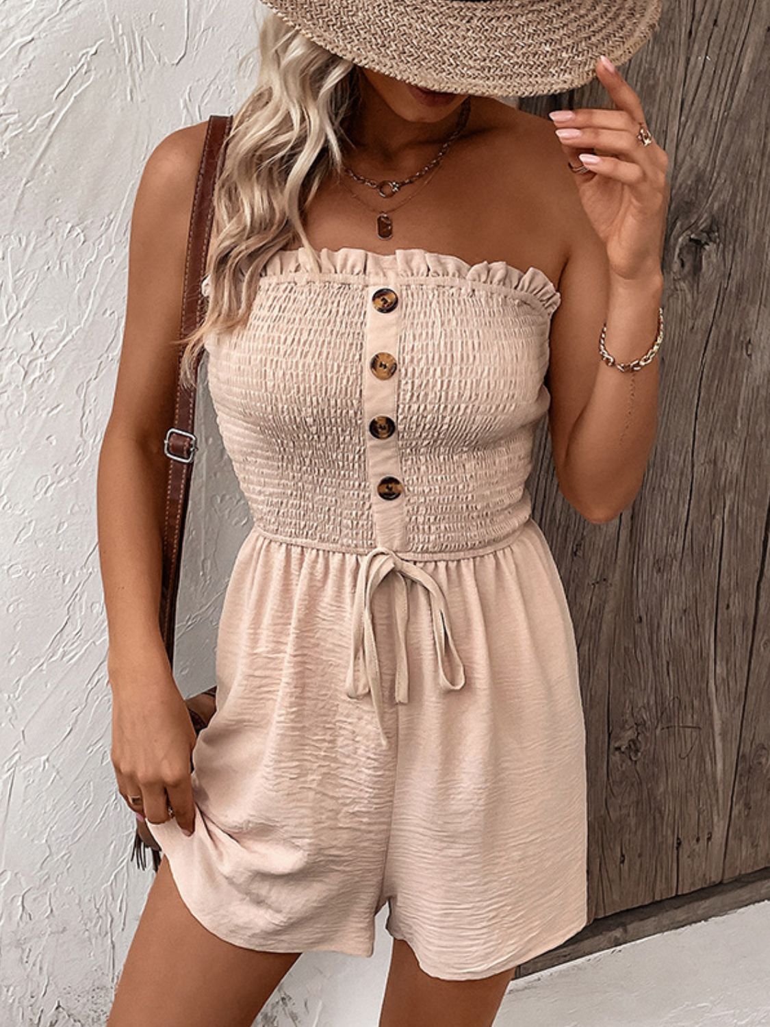 Tan smocked bodice romper with button front and tie waist, styled with a straw hat.