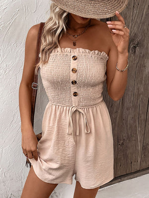 Tan smocked bodice romper with button front and tie waist, styled with a straw hat.