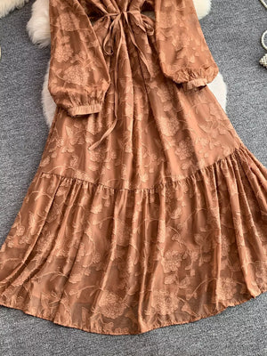 Rust embroidered tie-waist dress with tiered skirt and long sleeves.