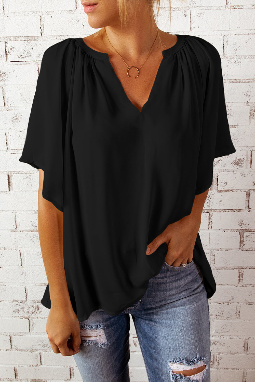 Black relaxed V-neck blouse with gathered neckline and cap sleeves, styled with jeans.