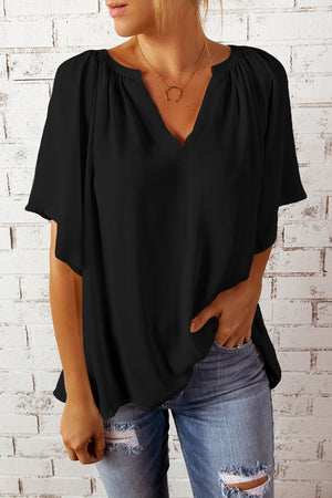 Black relaxed V-neck blouse with gathered neckline and cap sleeves, styled with jeans.