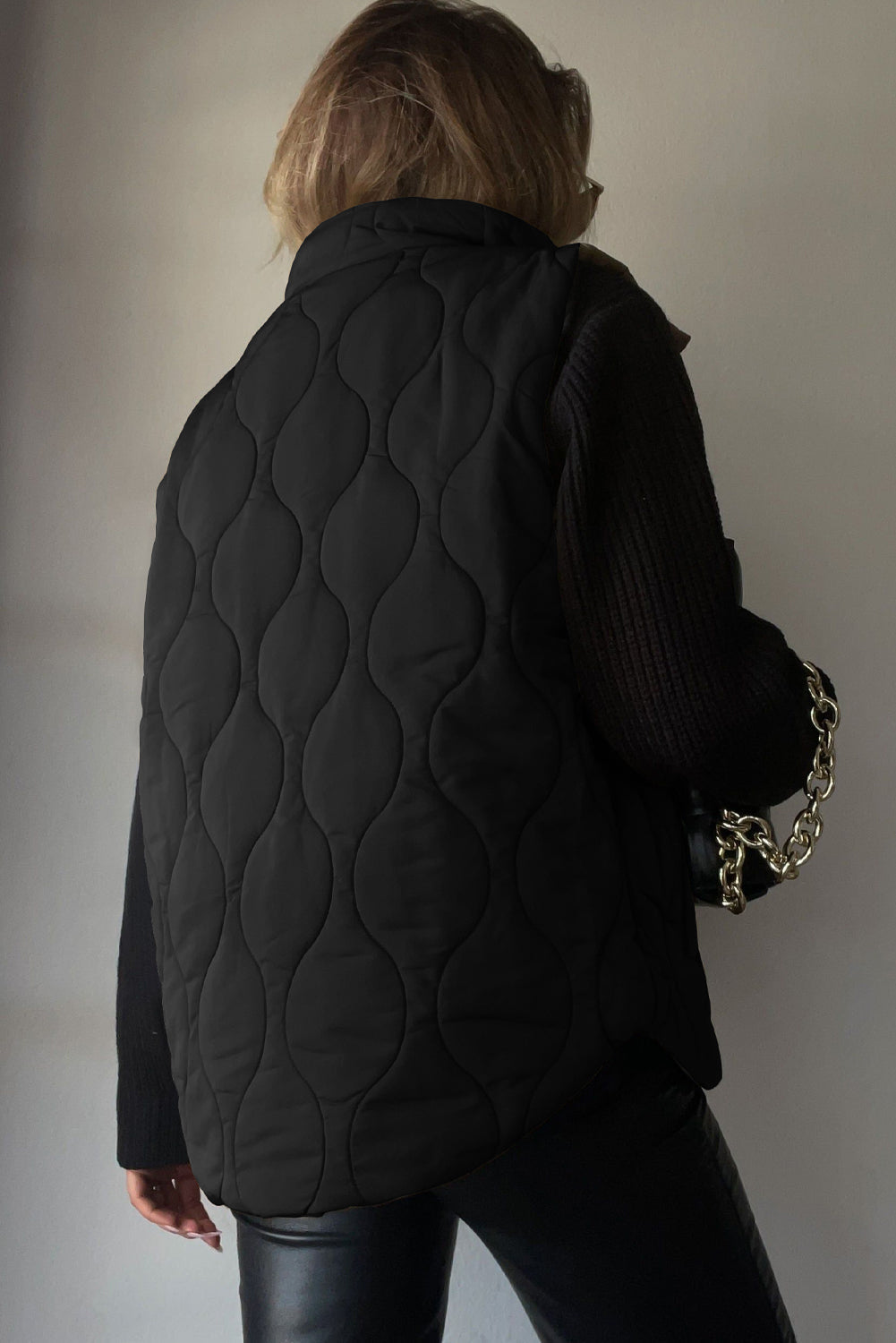 Black quilted stand-collar utility gilet with a wave pattern, worn over a black sweater.