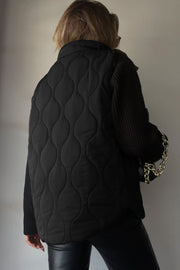 Black quilted stand-collar utility gilet with a wave pattern, worn over a black sweater.
