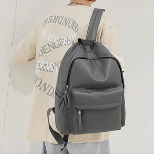 Dark gray minimalist leather backpack with front pocket and zipper details.