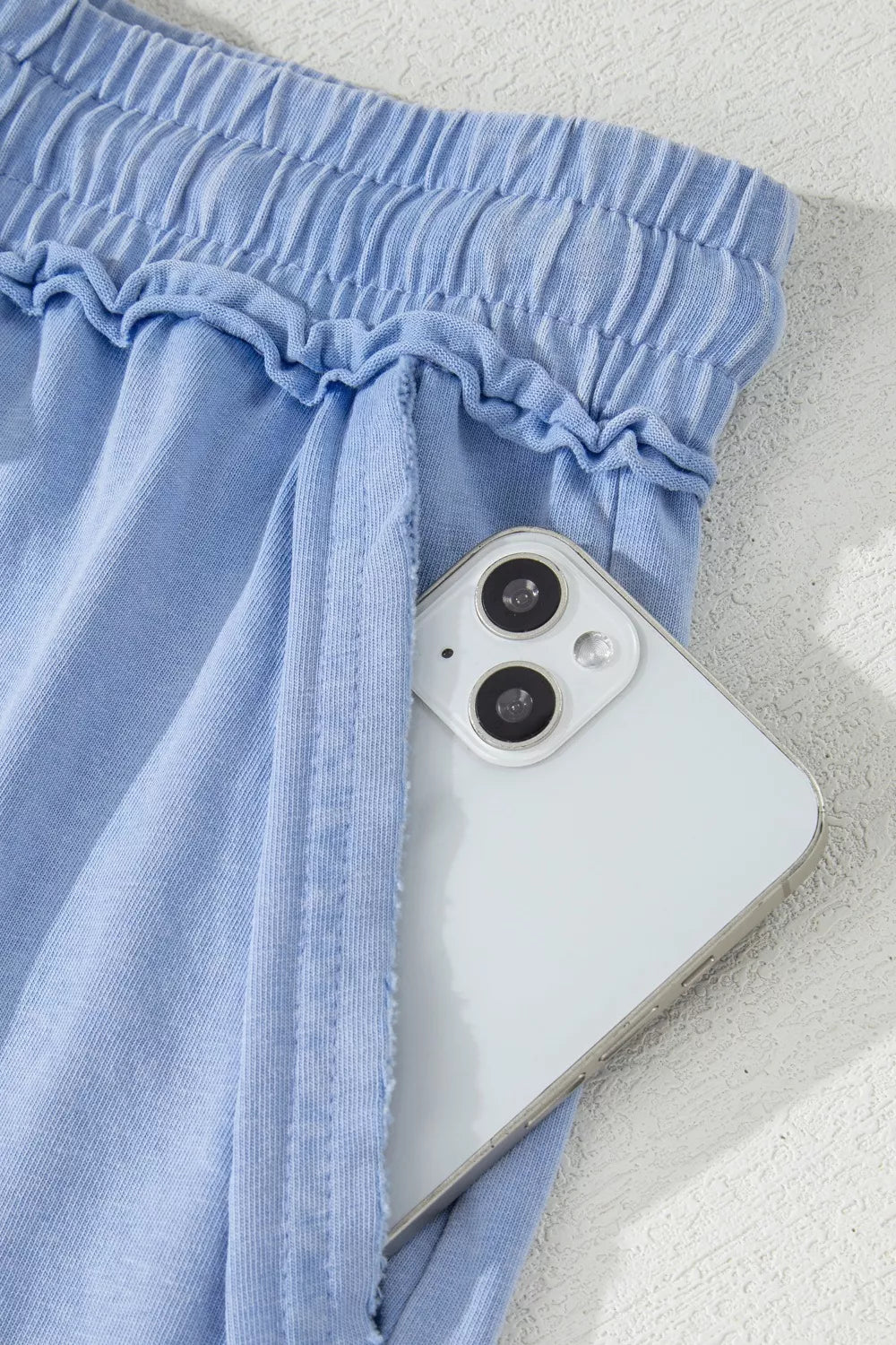 Light blue cotton drawstring shorts with pockets, showing a phone in the pocket.