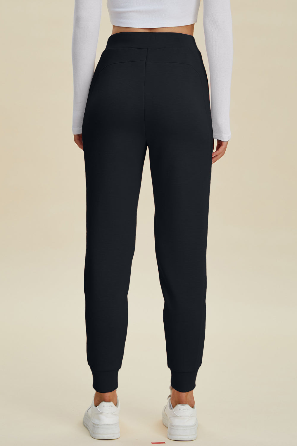 Black joggers with cuffed ankles and a relaxed fit, styled with a white long-sleeve top and sneakers.