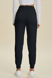 Black joggers with cuffed ankles and a relaxed fit, styled with a white long-sleeve top and sneakers.