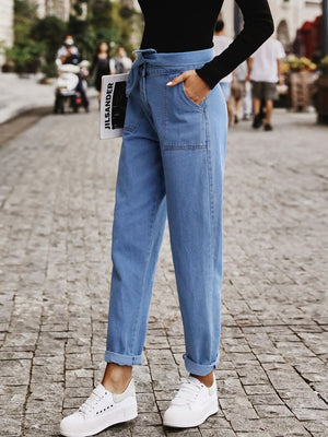 Belted high-waist light wash denim barrel trousers with cuffed hems.