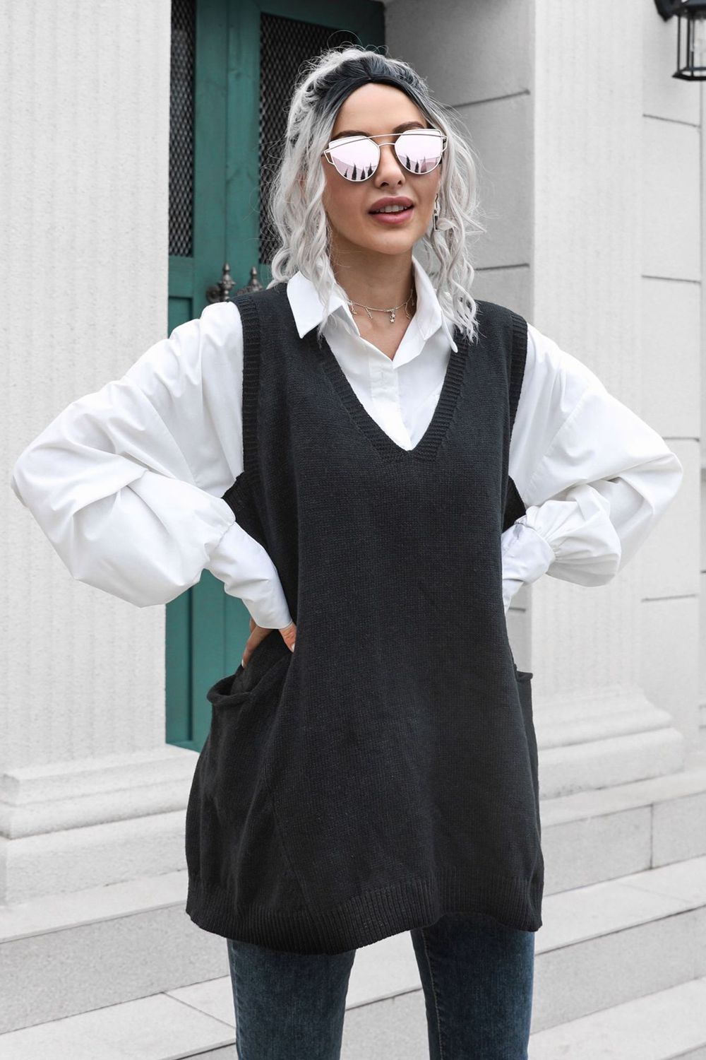 Black oversized knit vest with V-neck and front pockets, styled over a white shirt.