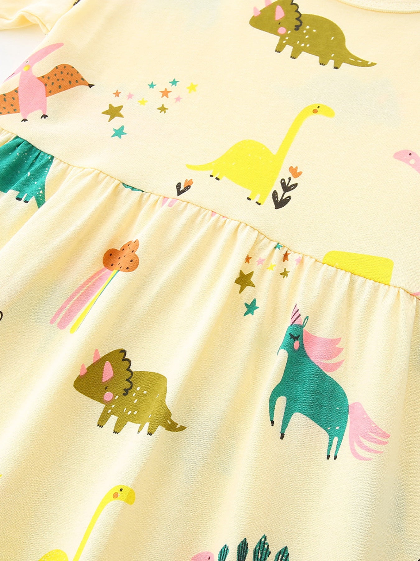 Yellow cotton toddler dress with whimsical dinosaur and unicorn print, ruffled waist detail.