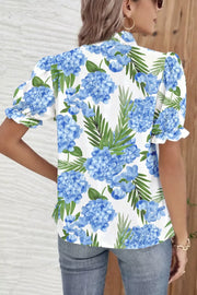 White blouse with blue hydrangea floral print, puff sleeves, and ruffled cuffs.