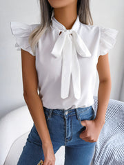 White ruffled sleeve pussybow blouse with a tie neck, styled with blue jeans.