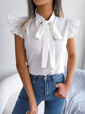 White ruffled sleeve pussybow blouse with a tie neck, styled with blue jeans.