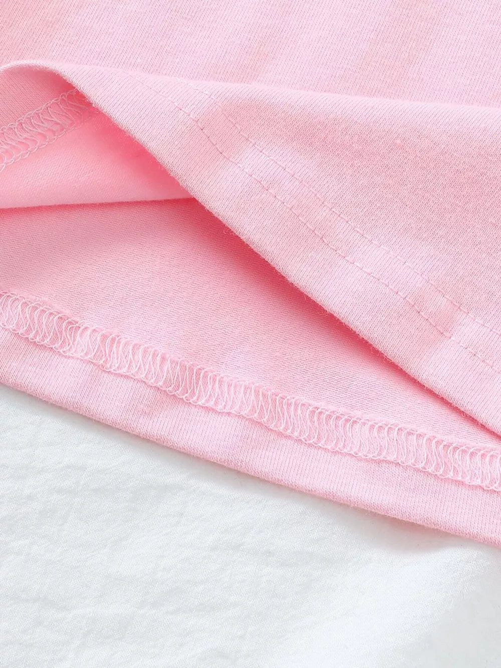 Pink cotton polo shirt hem detail with strawberry embroidery visible.