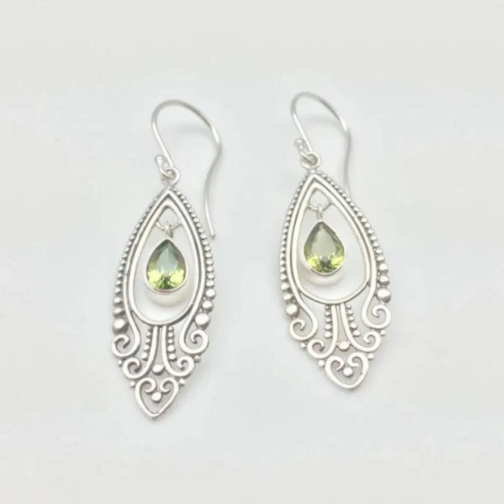 Silver filigree drop earrings with peridot gemstones and ornate scroll details.