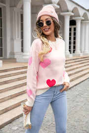 Blush pink intarsia knit crewneck sweater with red and pink hearts, cream trim, and a casual fit.