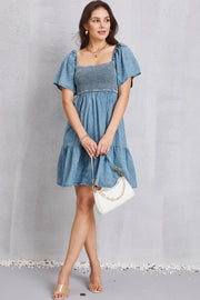 Light blue denim prairie dress with smocked bodice, puff sleeves, and tiered skirt.
