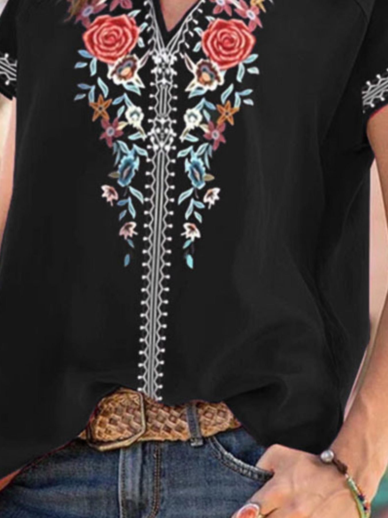 Black blouse with floral embroidery and notched neckline, styled with jeans and a belt.