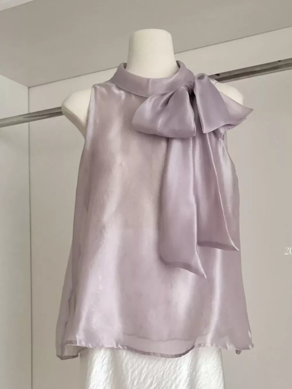 Sleeveless purple shirt with a large bow detail on the neckline, made of sheer fabric.