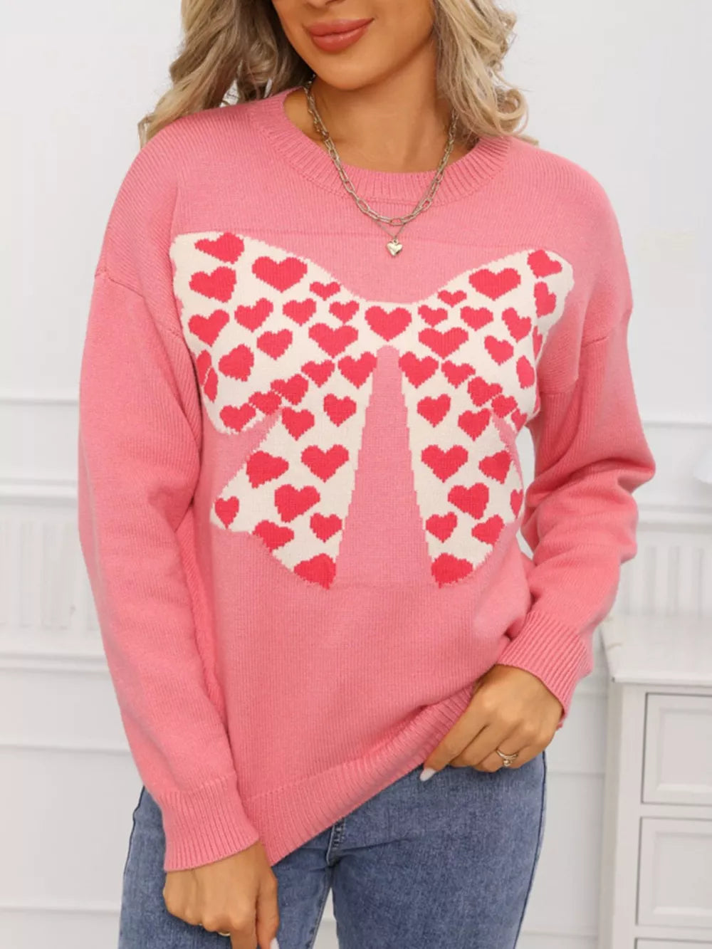 Pink acrylic sweater with a large heart bow graphic and round neck.