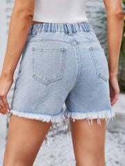 Light wash denim shorts with frayed hem and embellished fringe detail.