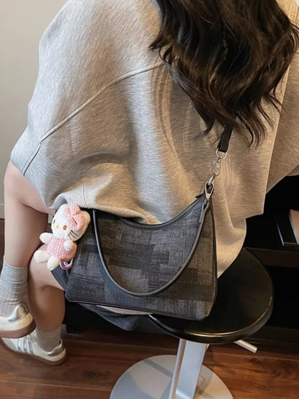 Crescent mini shoulder bag in black pu leather with textured pattern, worn with a Hello Kitty charm.