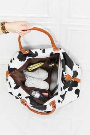 Cowhide print duffel bag with brown leather handles, packed with shoes, laptop, and accessories.
