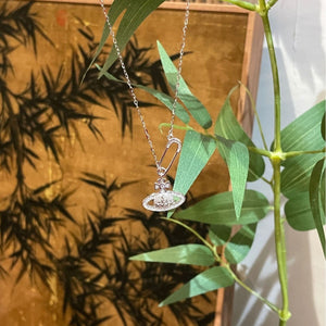 Silver necklace with orb pendant and safety pin charm, adorned with sparkling stones.