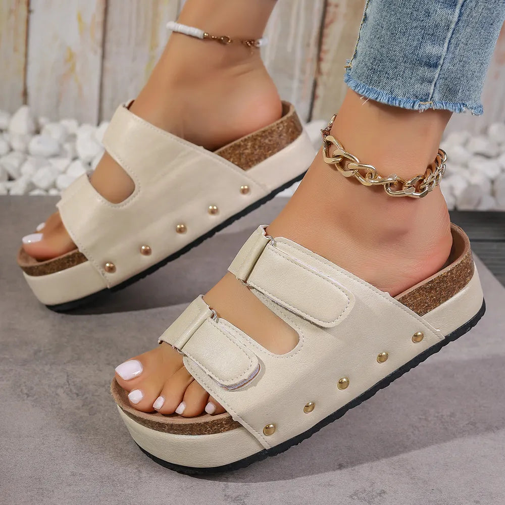 Beige platform sandals with double buckle straps and gold stud details.