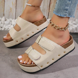 Beige platform sandals with double buckle straps and gold stud details.