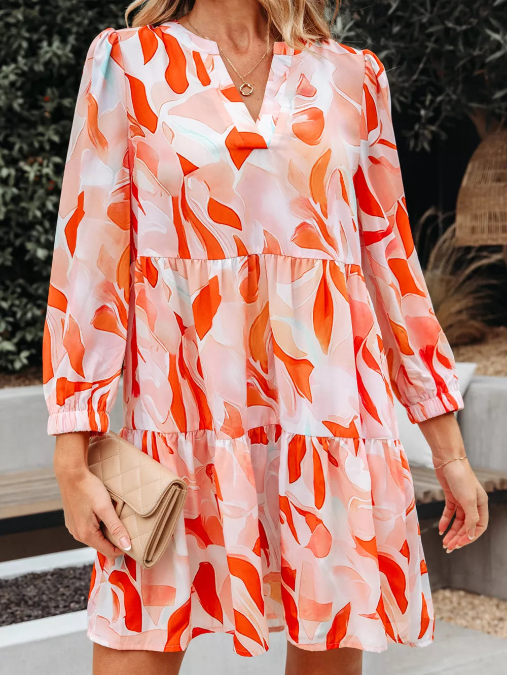 Vibrant abstract print tiered mini dress with V-neck and long sleeves.