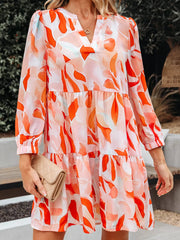 Vibrant abstract print tiered mini dress with V-neck and long sleeves.