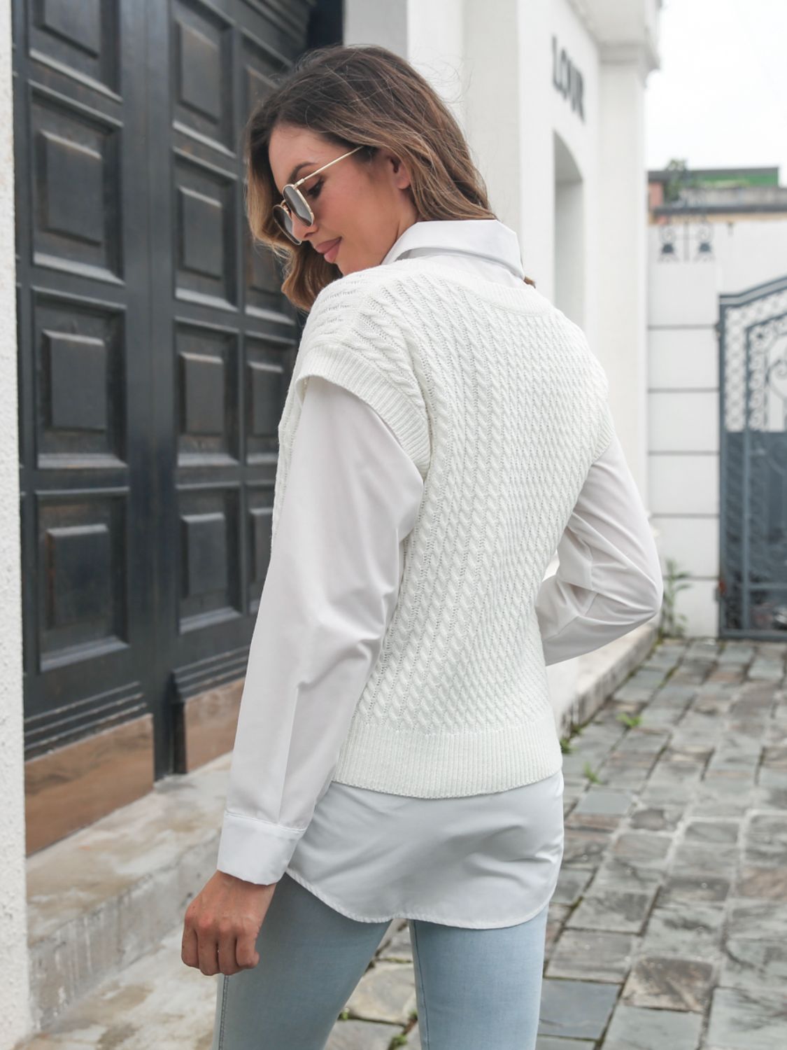 White cable knit V-neck sleeveless sweater over a white button-up shirt.