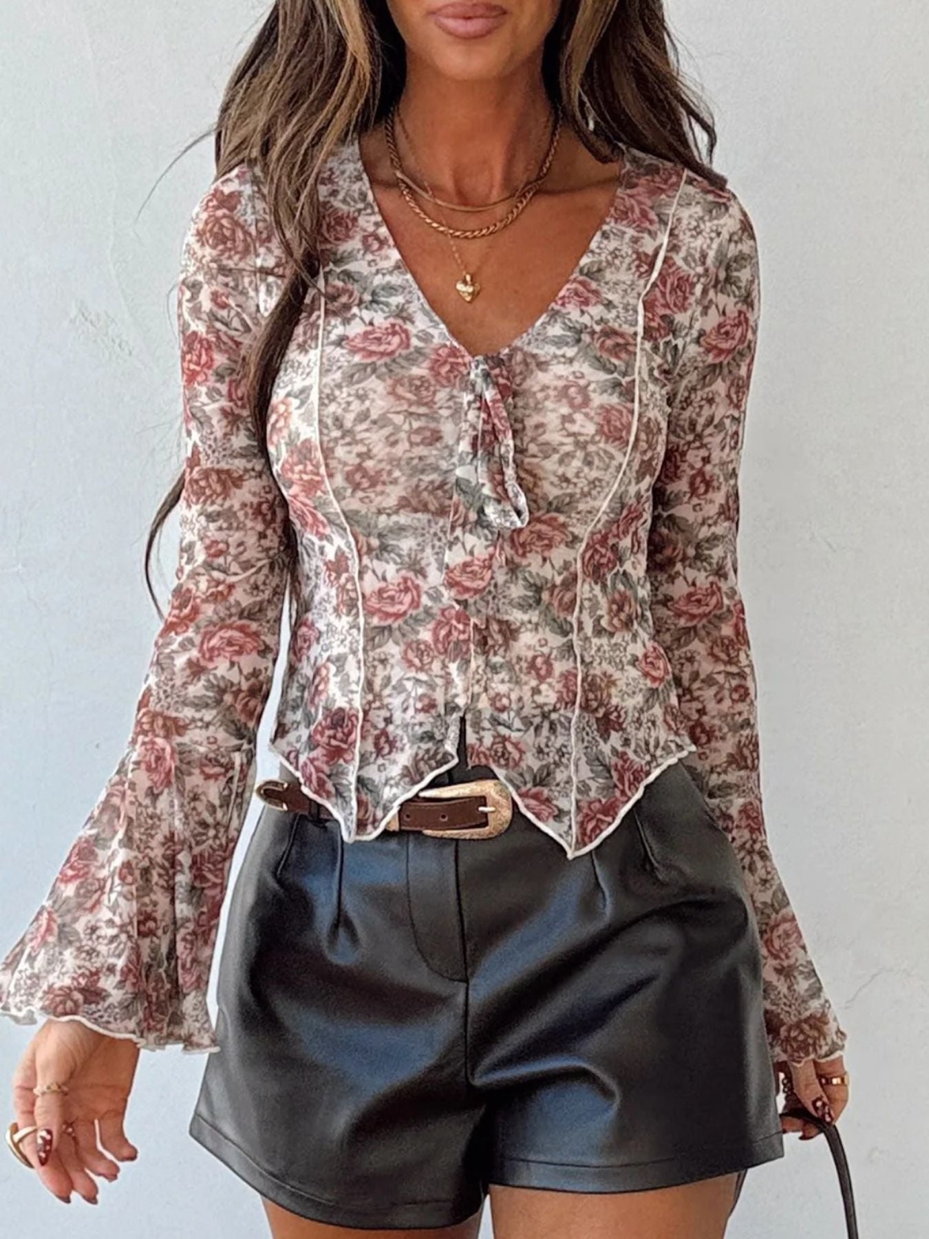 Charming floral print mesh blouse with tie-neck, long bell sleeves, and ruffled hem.