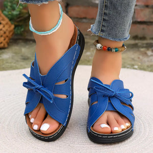 Blue criss-cross wedge sandals with bow detail and white stitching.