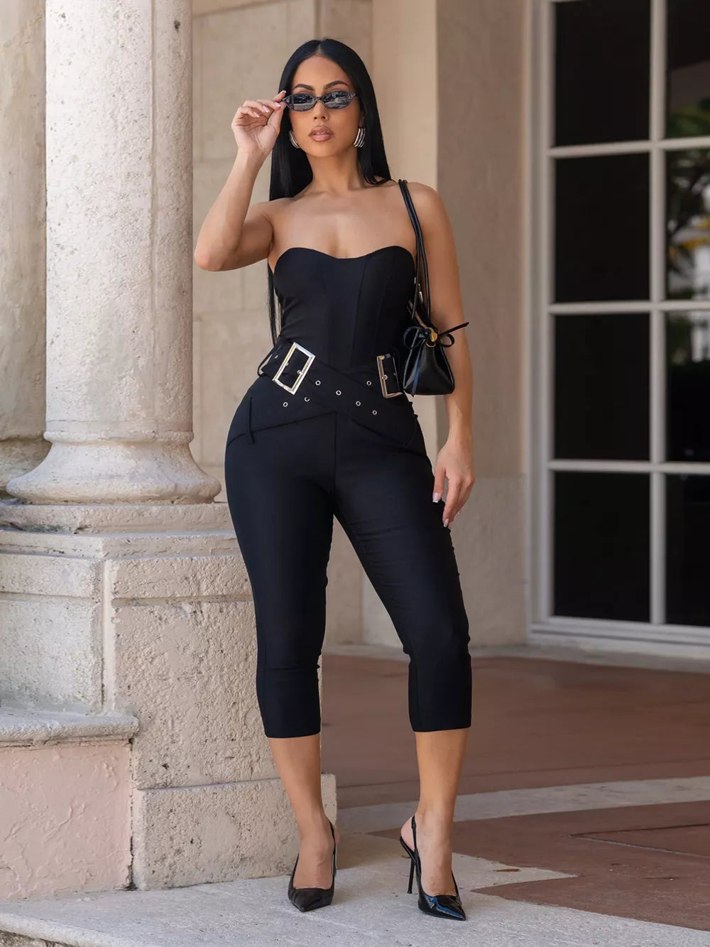 Black strapless jumpsuit with cinched waist, double buckle belt, and cropped pants.