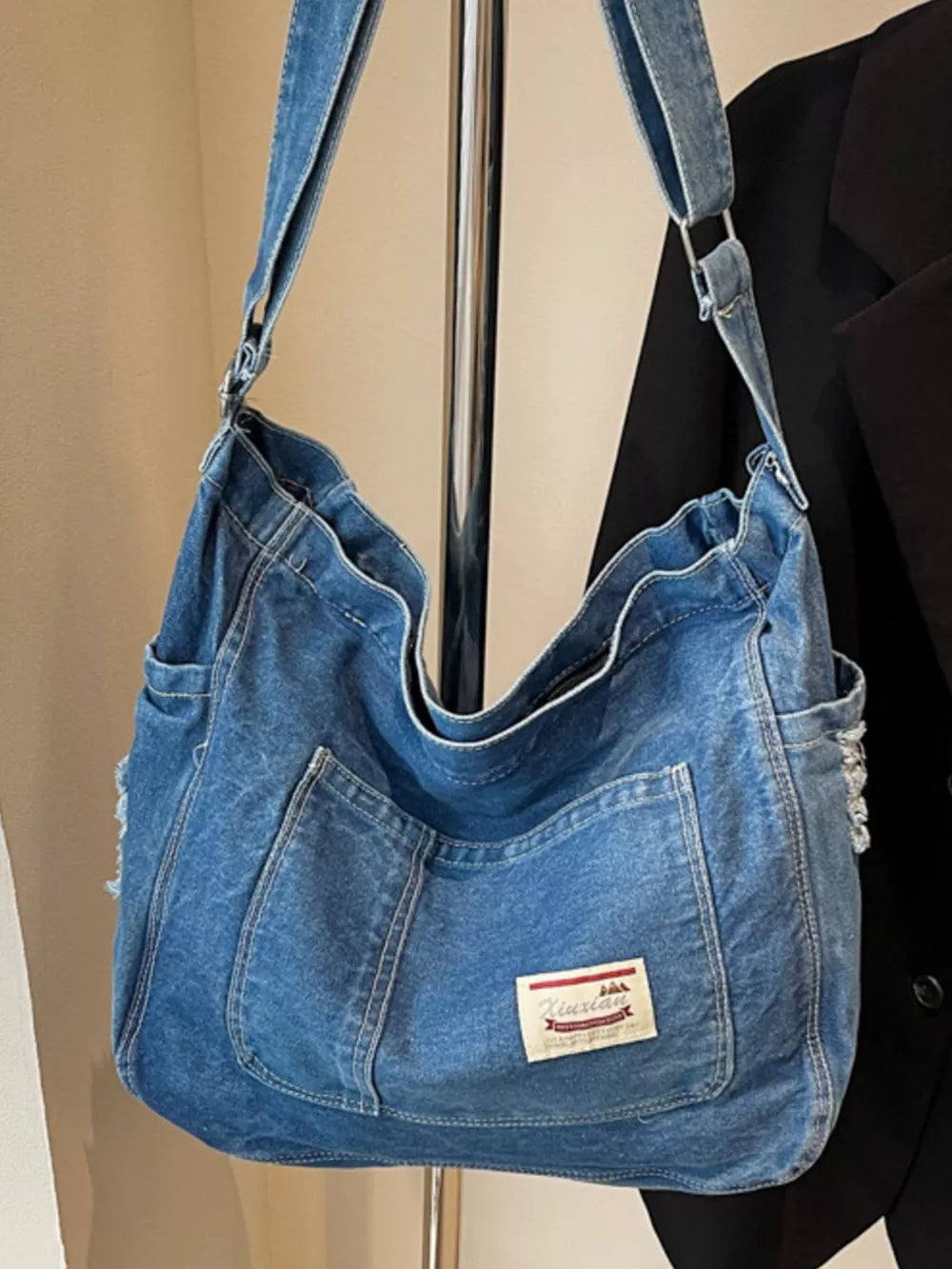 Slouchy blue denim crossbody bag with contrast stitching and exterior pockets.