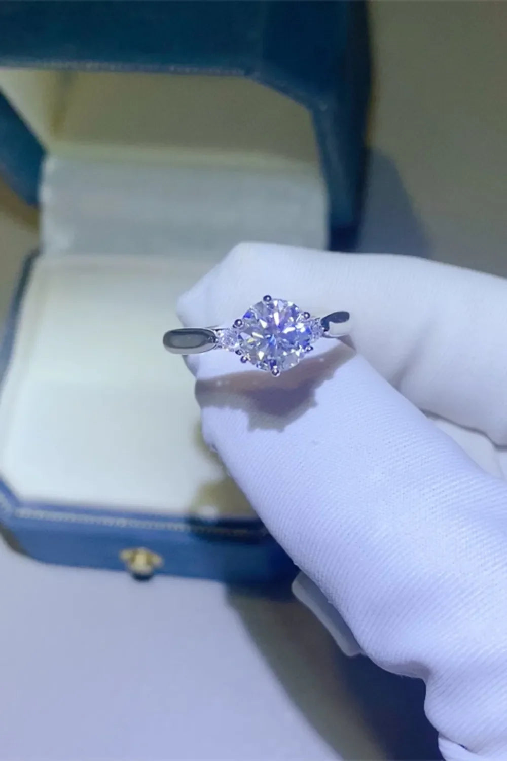 Silver moissanite trilogy engagement ring with a central round-cut stone and two smaller stones.