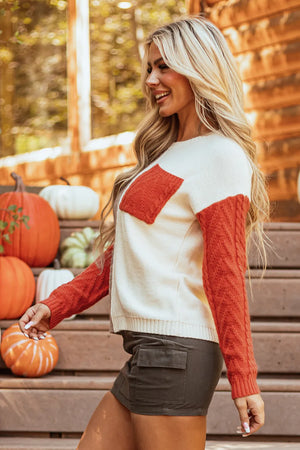 Textured panel pocket sweater in cream with orange sleeves and pocket detail.