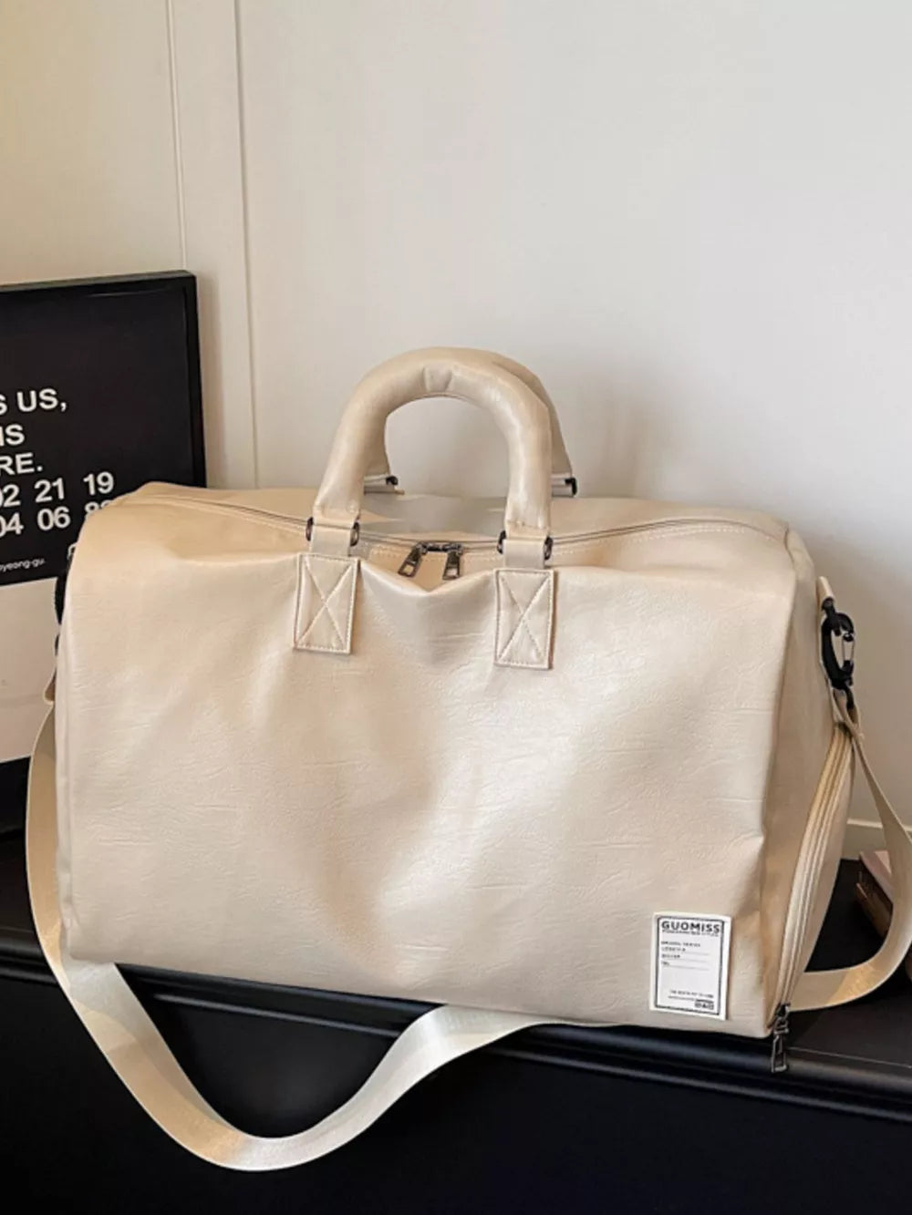 Off-white pu leather travel duffel bag with top handles and adjustable shoulder strap.