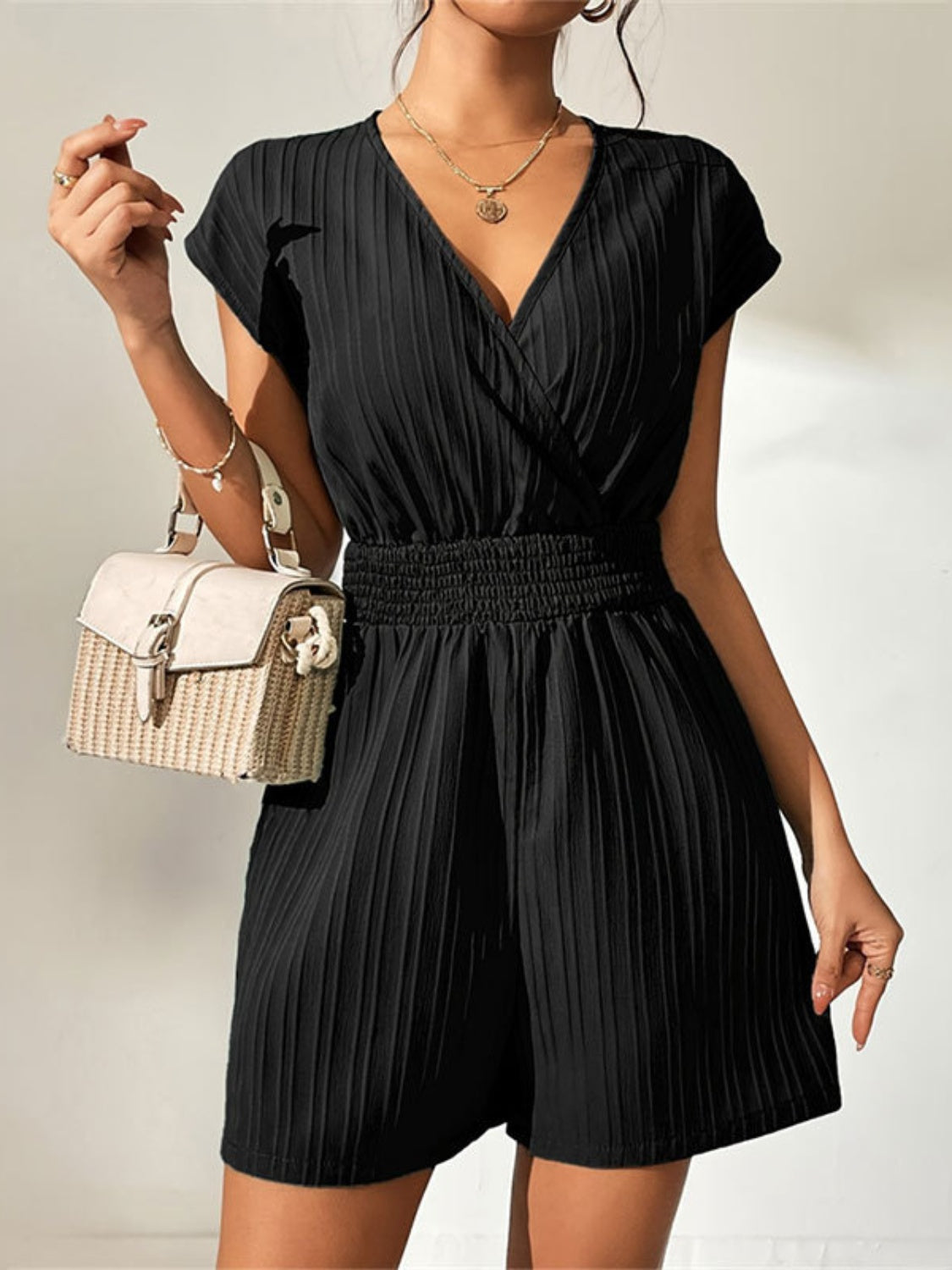 Black textured wrap romper with smocked waist and short sleeves.