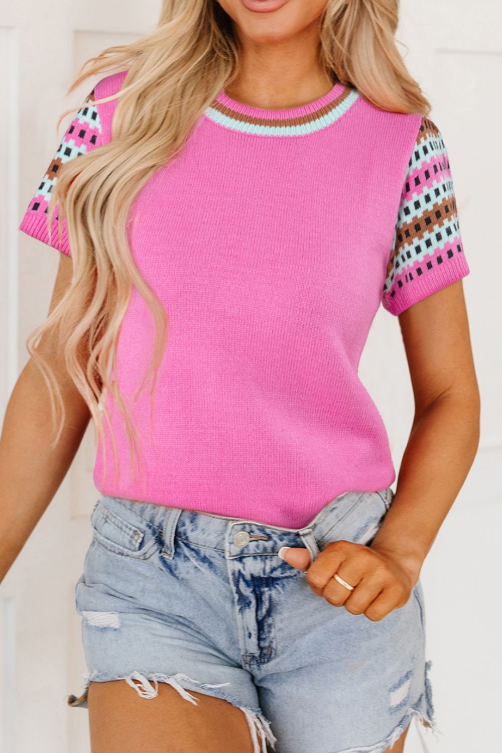 Fuchsia pink knit top with geometric patterned sleeves and striped neckline.
