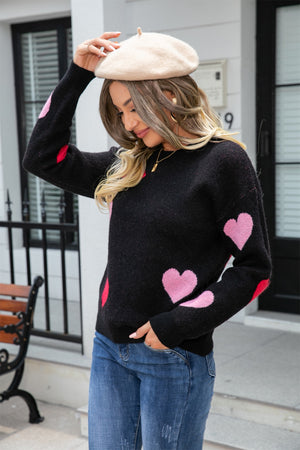 Black crewneck sweater with pink and red intarsia hearts, long sleeves.